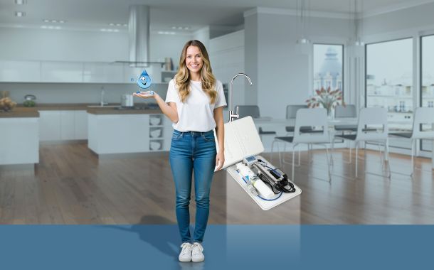 Sistema Home Water System Acquaviva per la microfiltrazione dell’acqua domestica con ragazza in cucina e dispositivo sottolavello plastic free